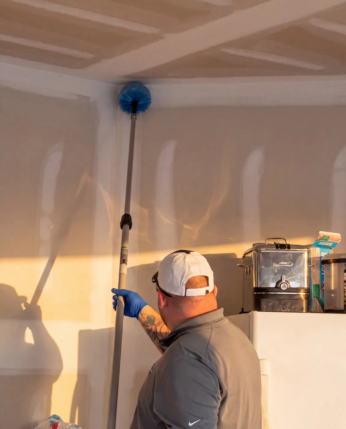 A Blue Jays technician brushing cobwebs from an interior ceiling corner